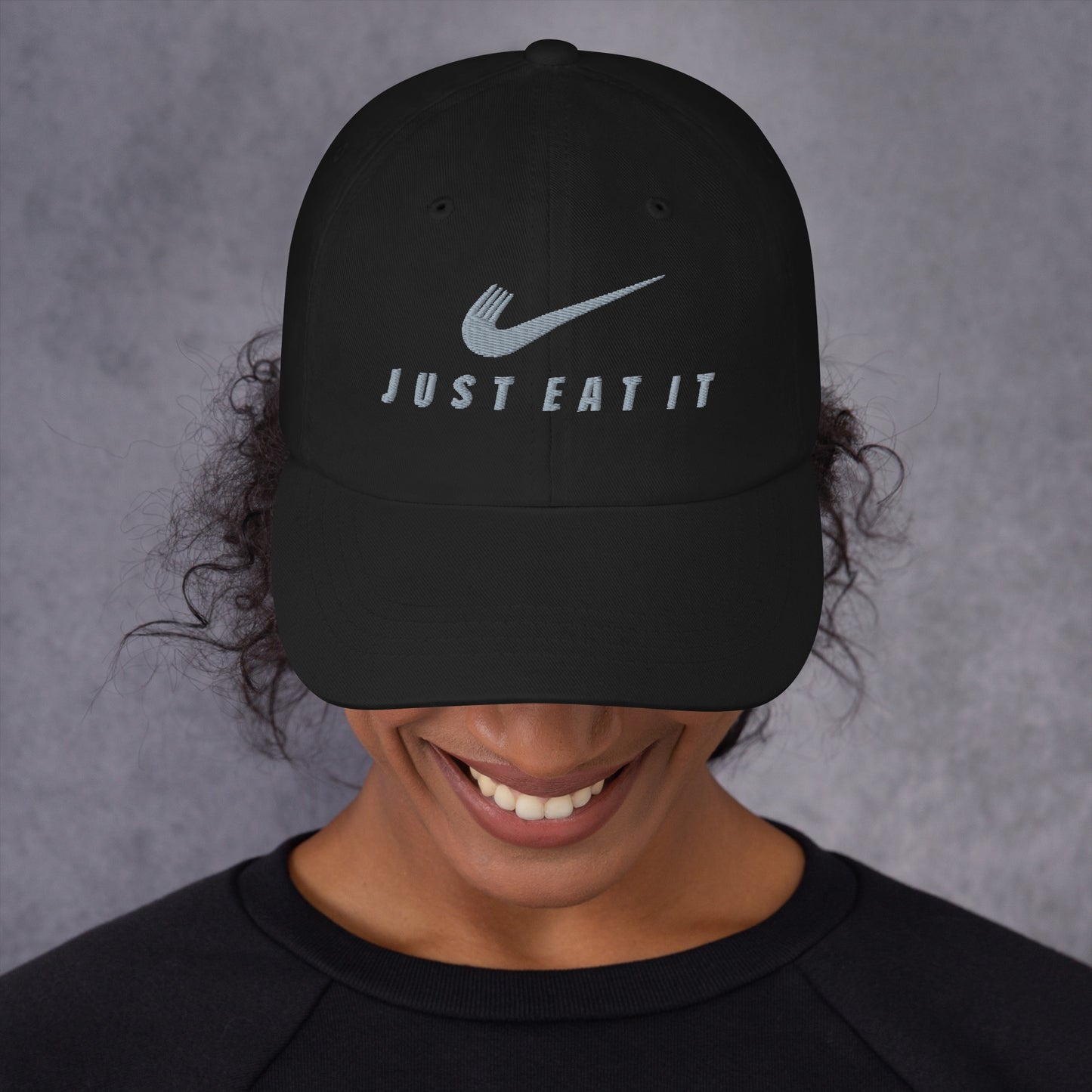 Black dad hat featuring a parody Nike logo and "Just Eat It" text, from Appetite Apparel with a classic curved brim.